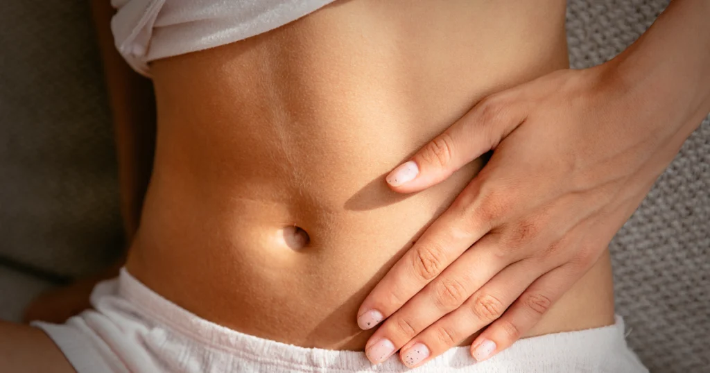 Kobieta dotyka brzucha, podkreślając zdrowie i dobre samopoczucie.