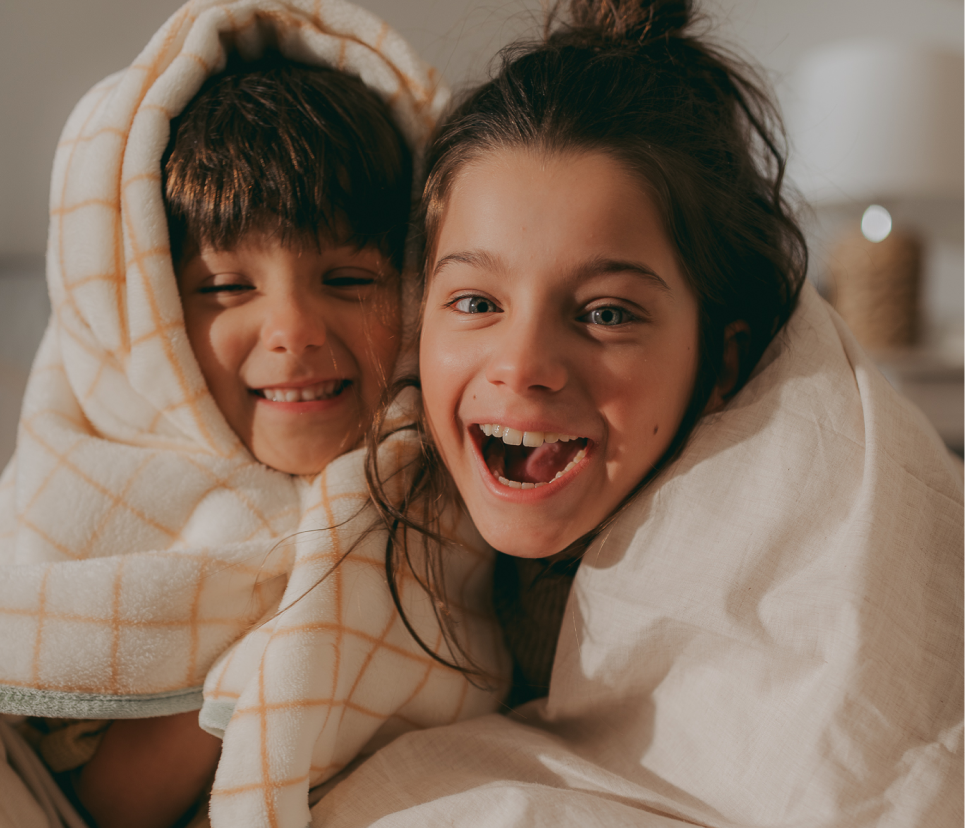 Dwoje szczęśliwych dzieci otulonych kocami, promieniujących zdrowiem i radością.